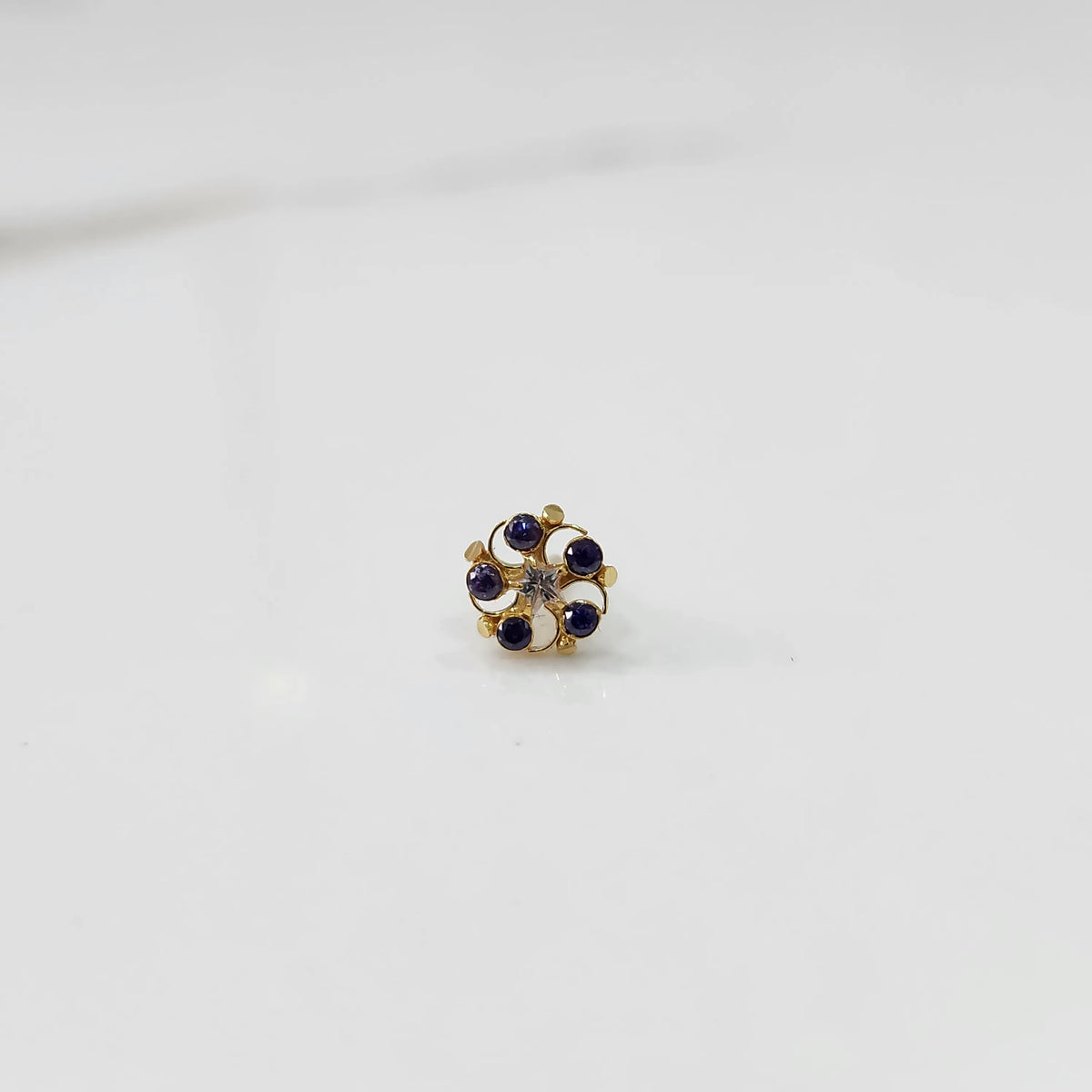 Gold nose pin with blue and white gemstone petals on white background