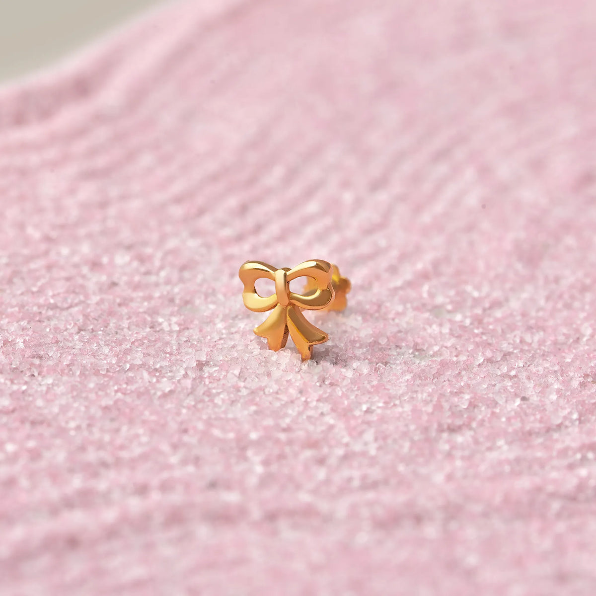 Gold bow-shaped ribbon nose stud on pink glitter background