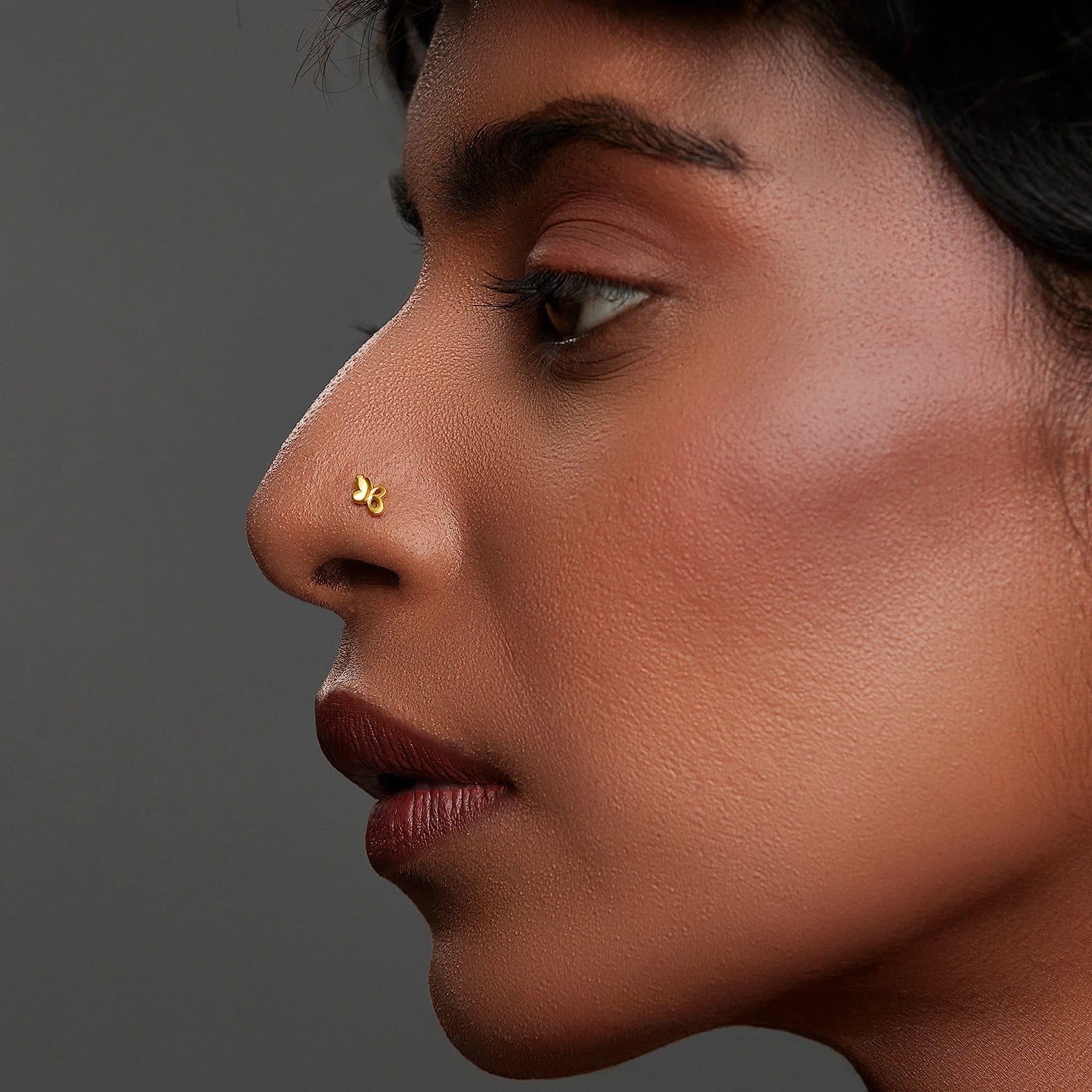 Side profile of woman wearing gold butterfly-shaped nose pin