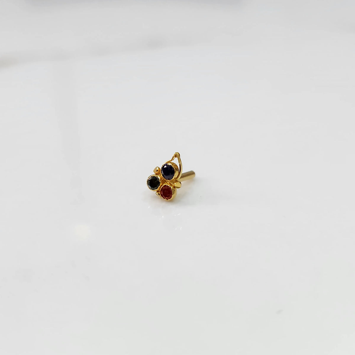 Gold butterfly-style nose pin with blue, black, and red stones, product shot