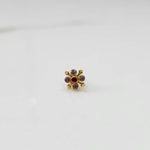 Gold nose pin with clear gemstone petals and red center stone, angled view on white background