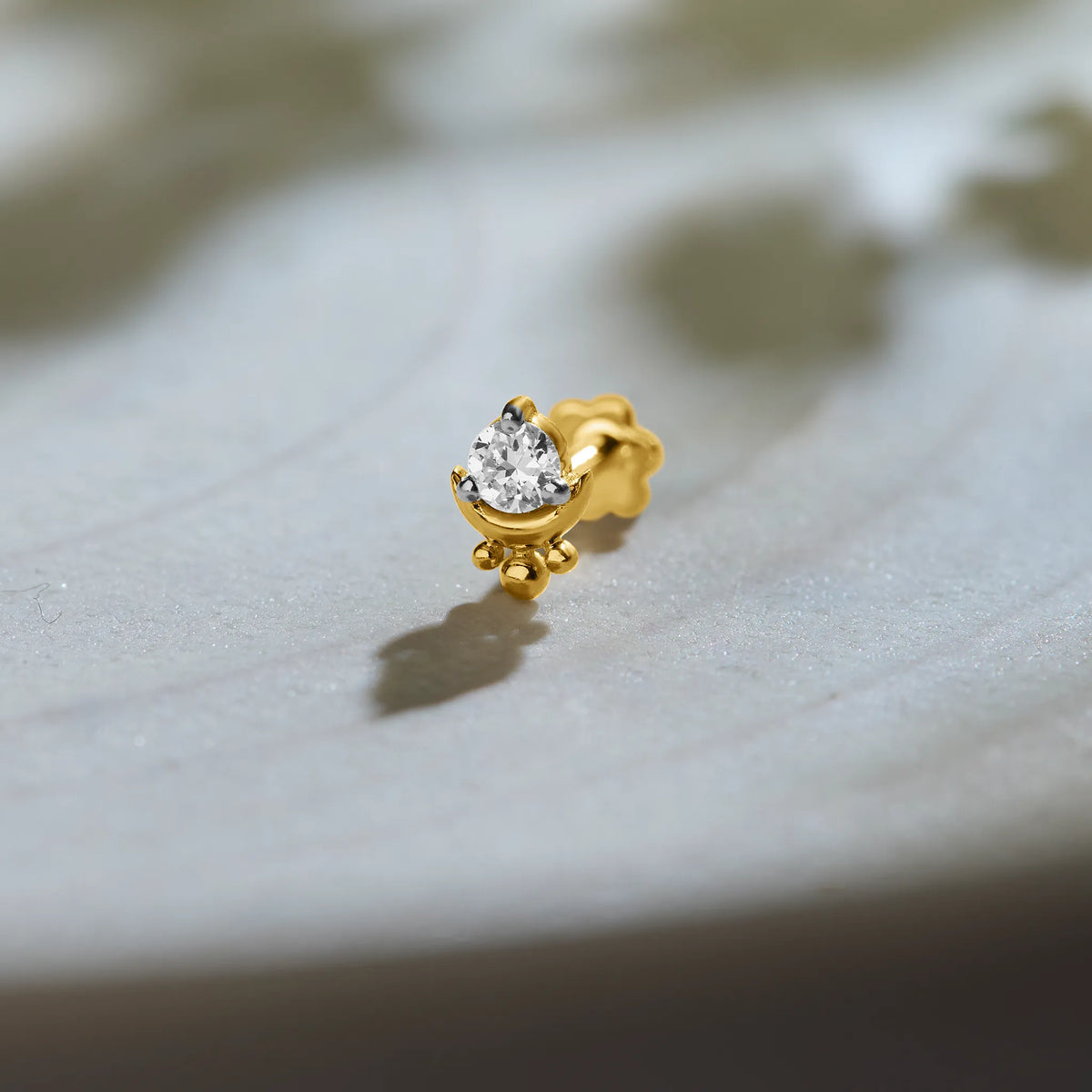 Single stone nose pin gold with round diamond solitaire in prong setting on soft grey background