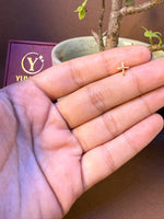 Simple cross-shaped gold nose pin held in hand, Yuvora jewelry box in background