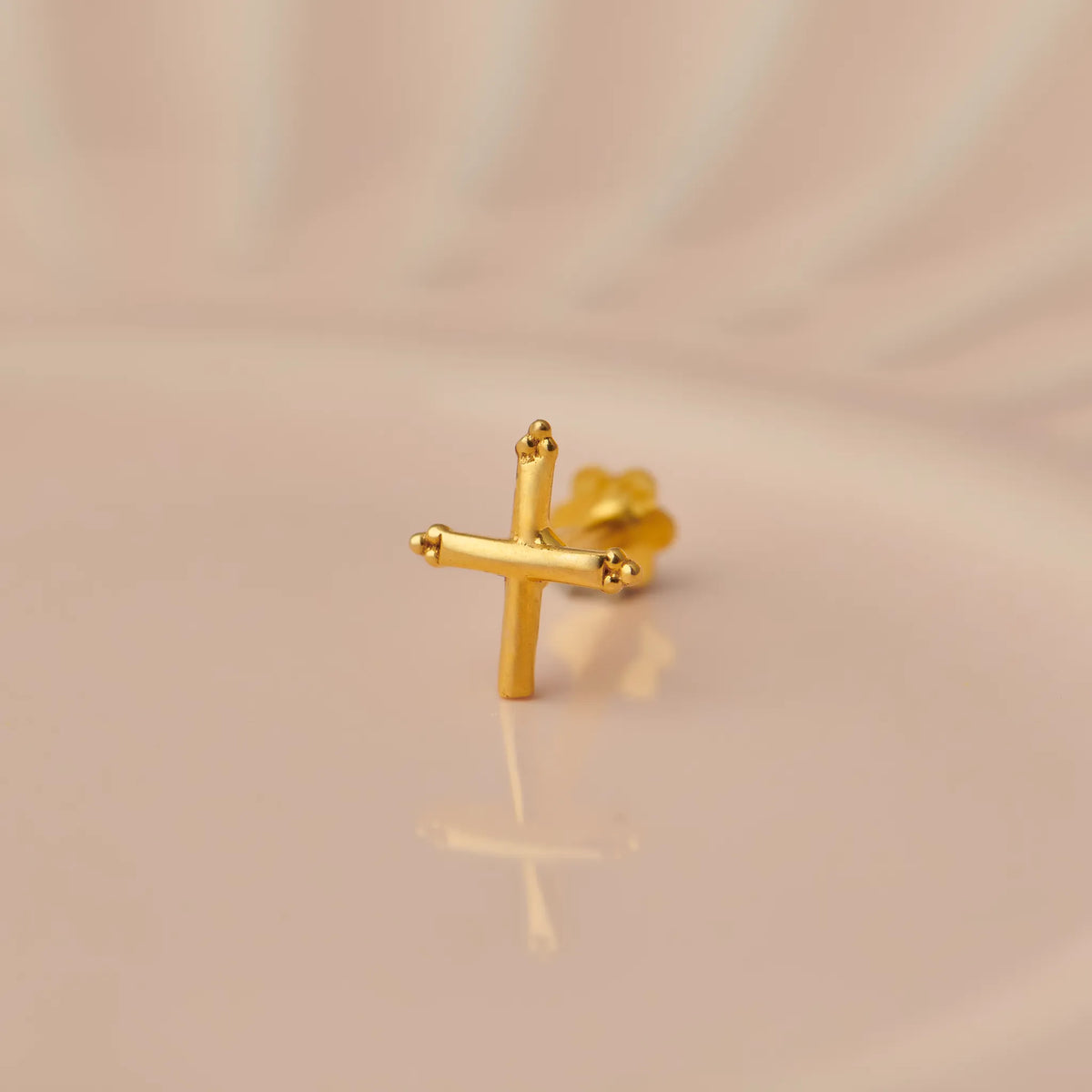 Gold cross-shaped nose stud with beaded tips on beige background