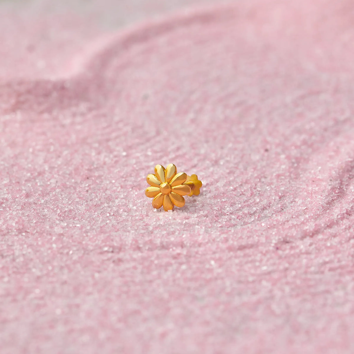 Gold daisy flower-shaped nose stud on pink glitter background