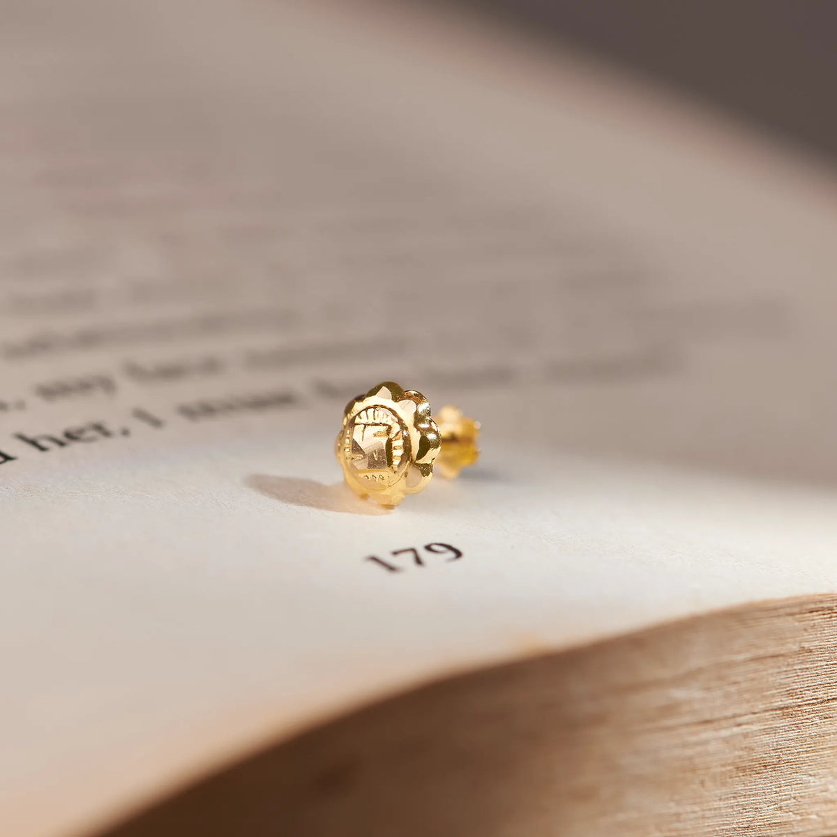 Gold textured flower stud earring, close-up on paper