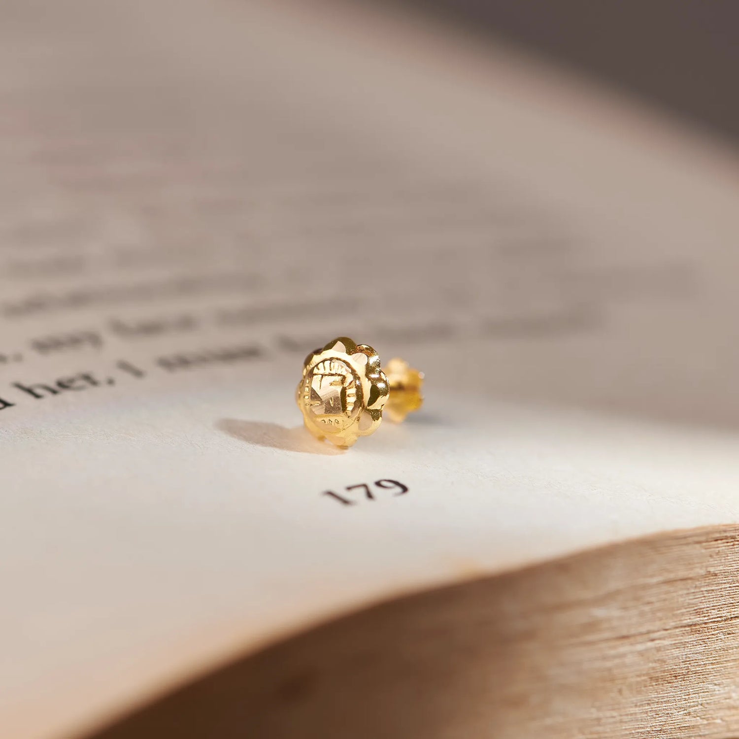 Gold textured flower stud earring, close-up on paper