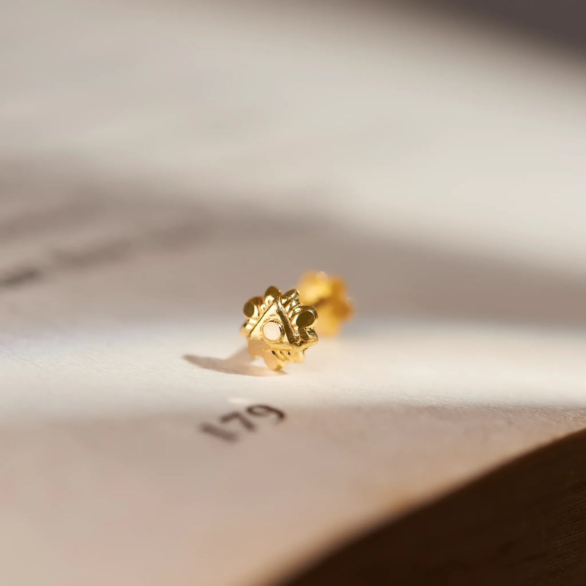 Gold faceted cluster stud earring, close-up on paper
