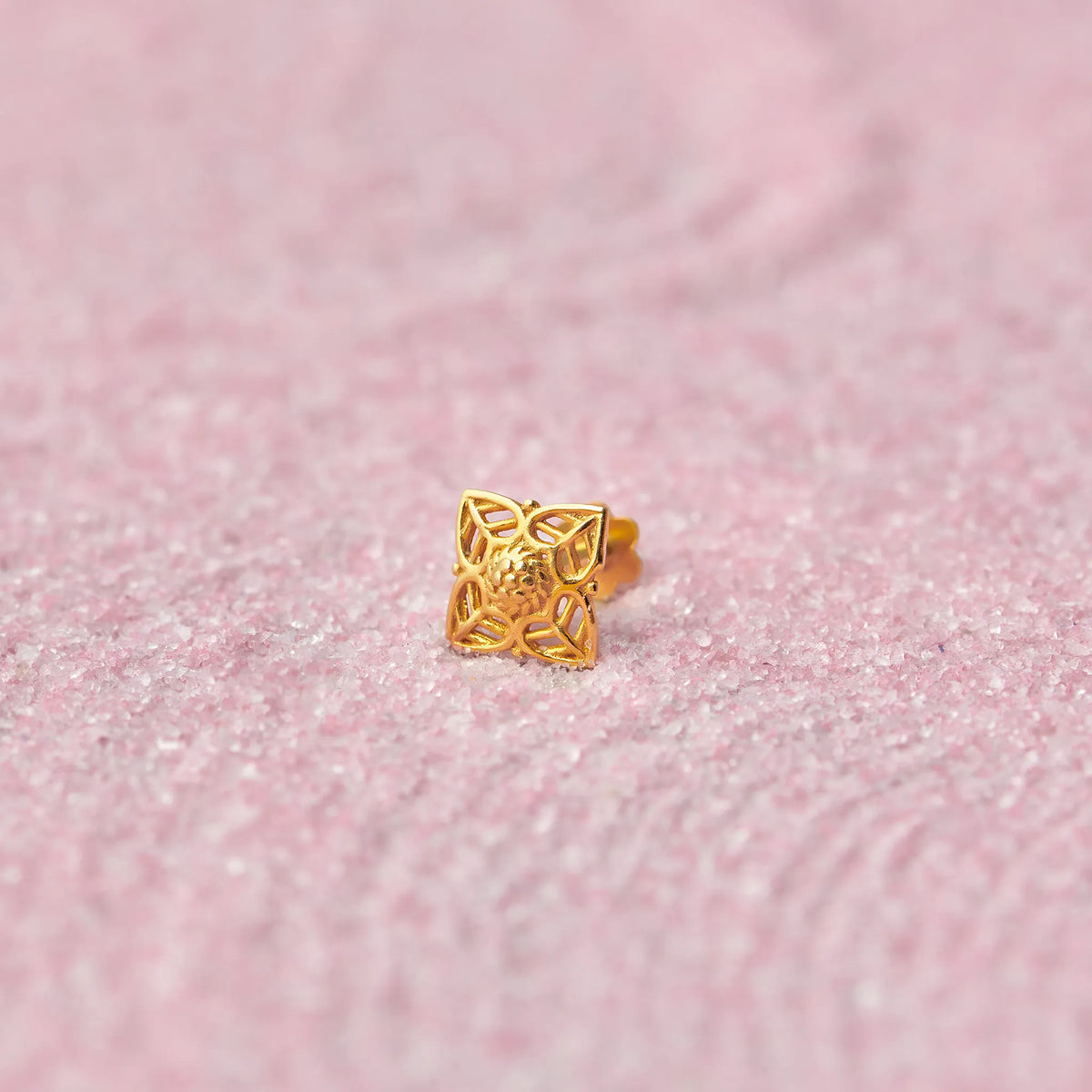Gold floral cutwork nose stud in diamond shape on pink glitter background