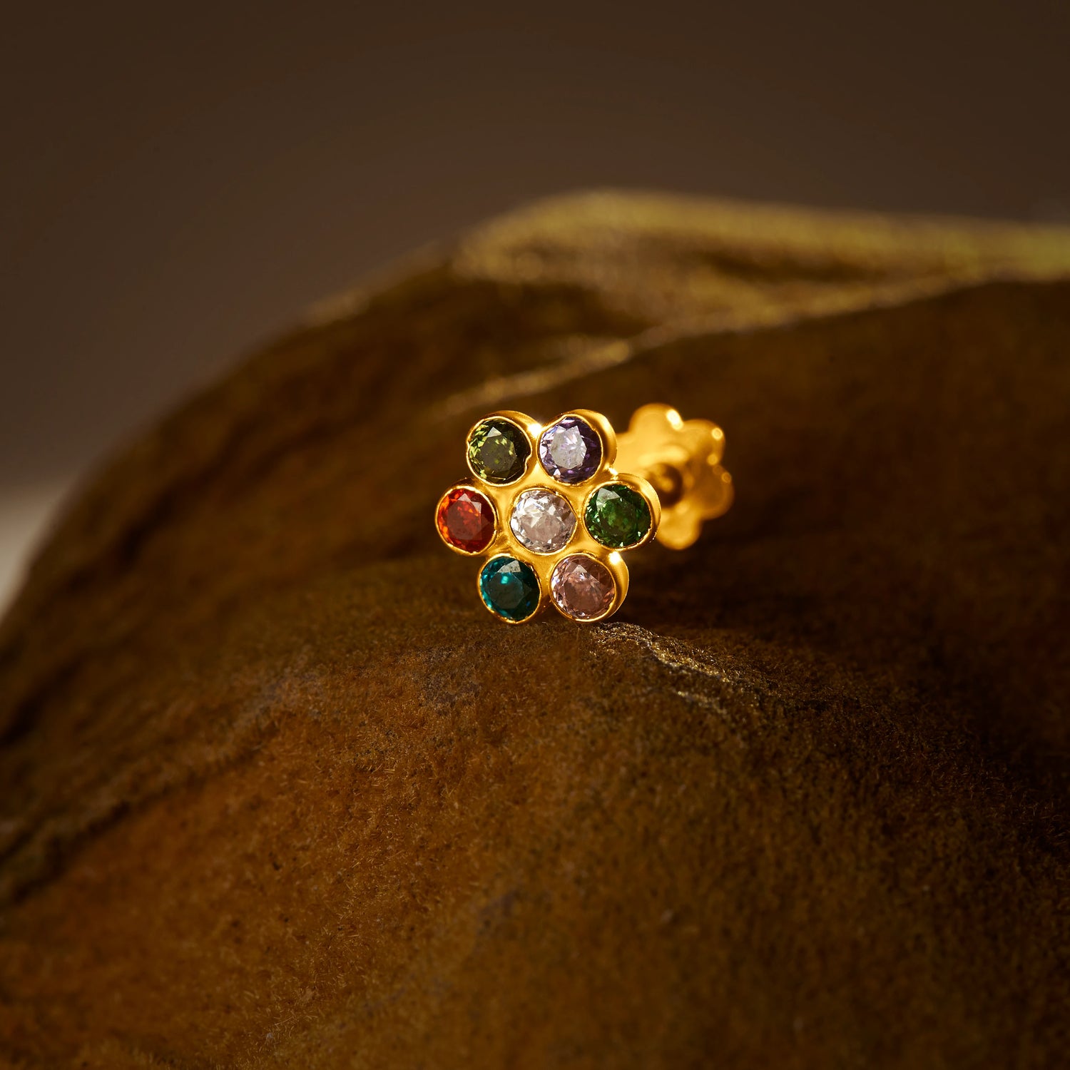 Nose pin design gold with multicolor floral stones on textured brown surface