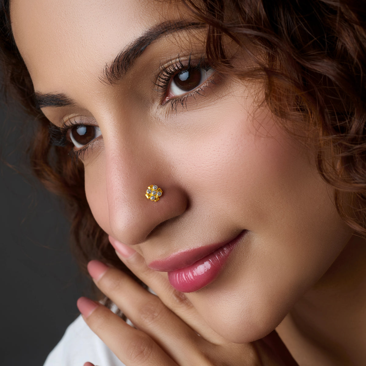 Woman wearing a floral gold nose pin, chin resting on hand