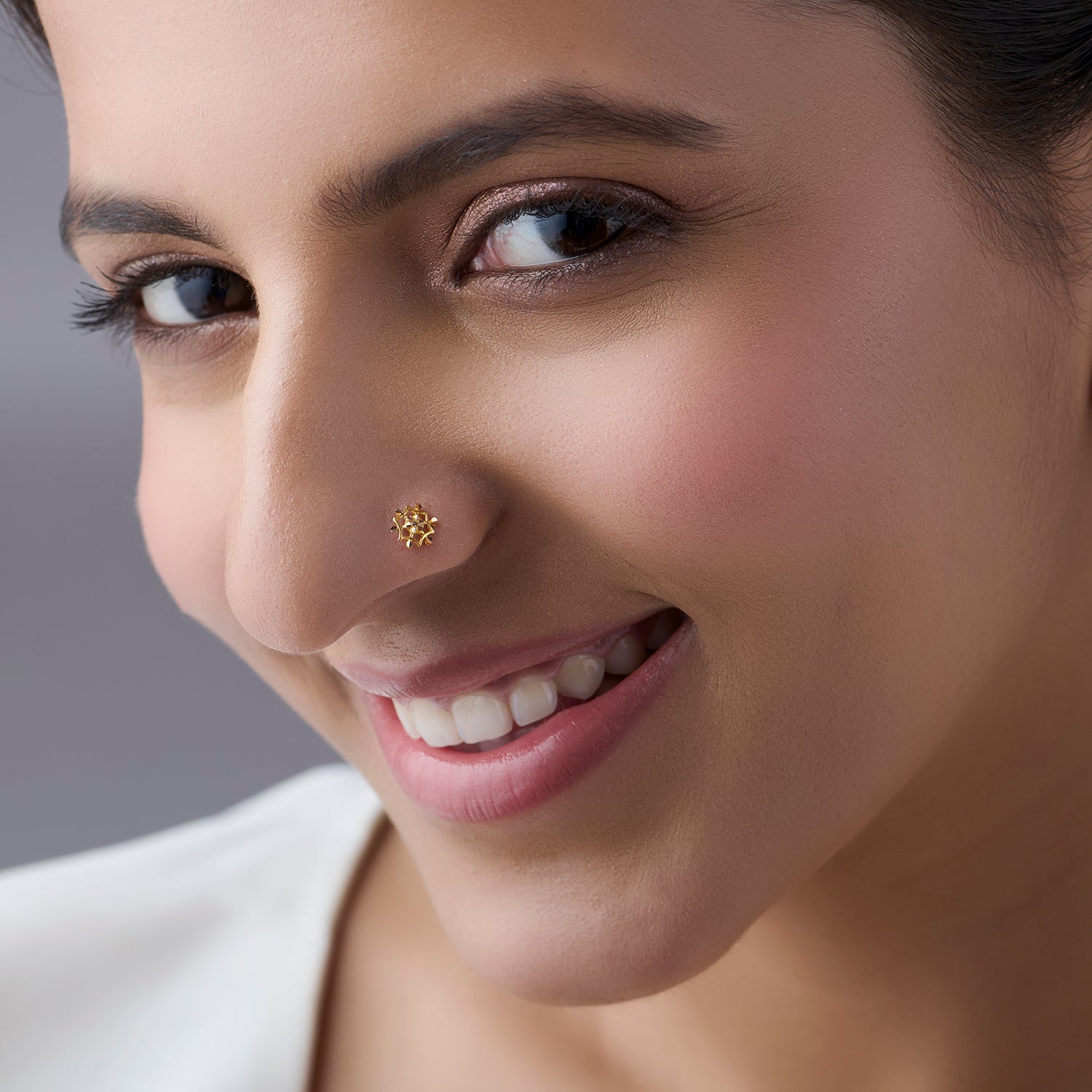 Front view of smiling woman wearing gold flower-shaped nose pin
