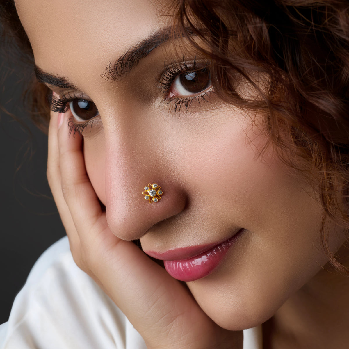 Woman wearing a floral gold nose pin, resting on hand