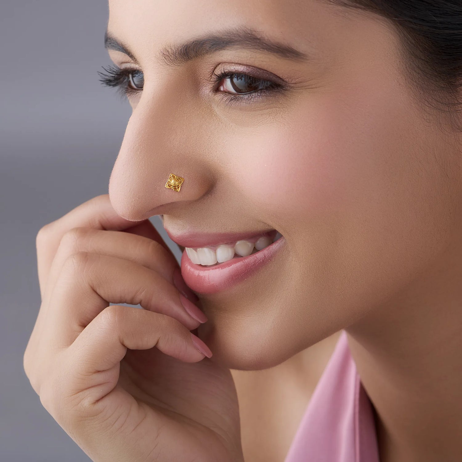 Side profile of a woman smiling, wearing a delicate gold flower nose stud