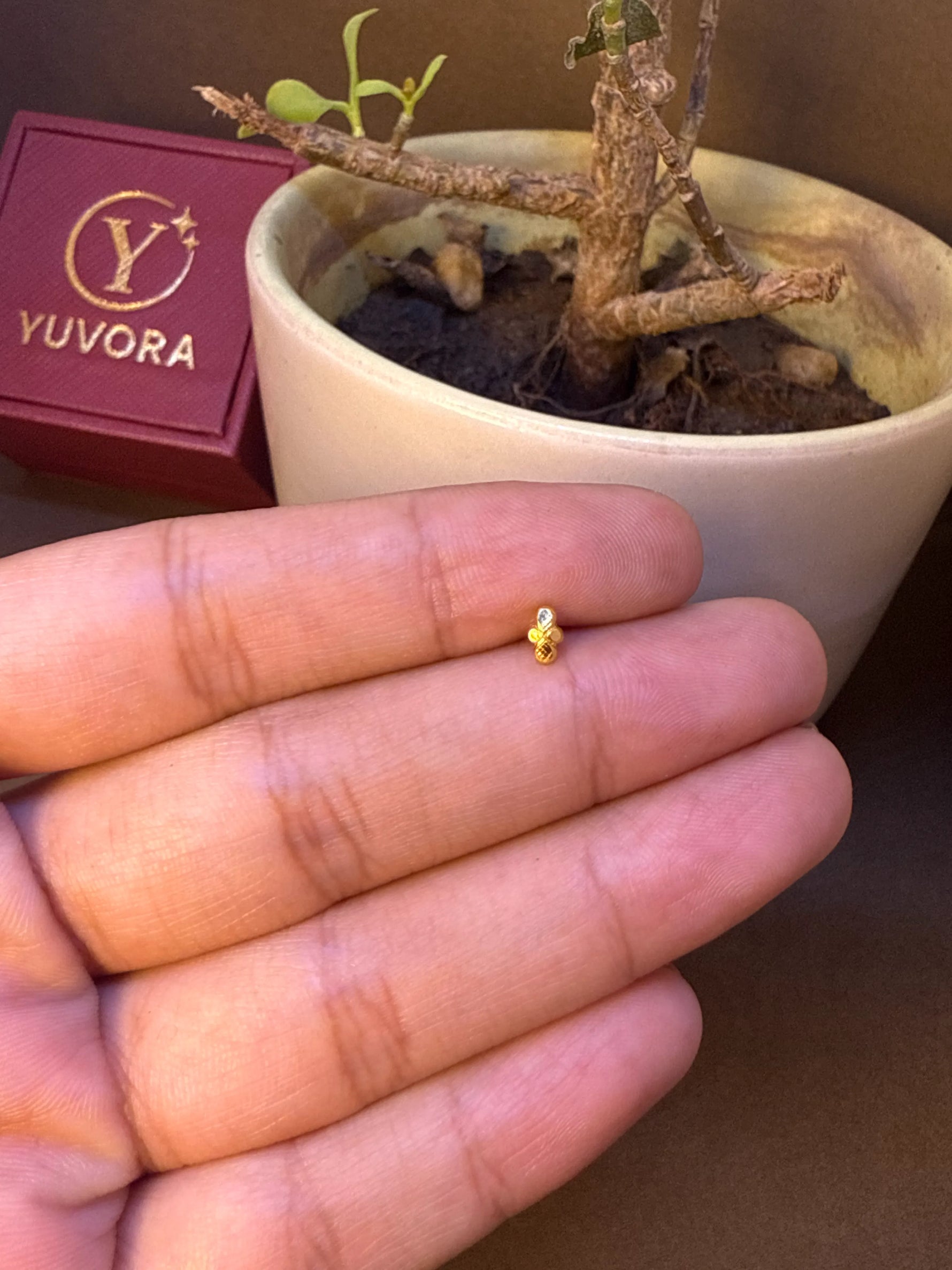 Close-up of small gold flower-shaped nose pin stud with white stone center on fingers