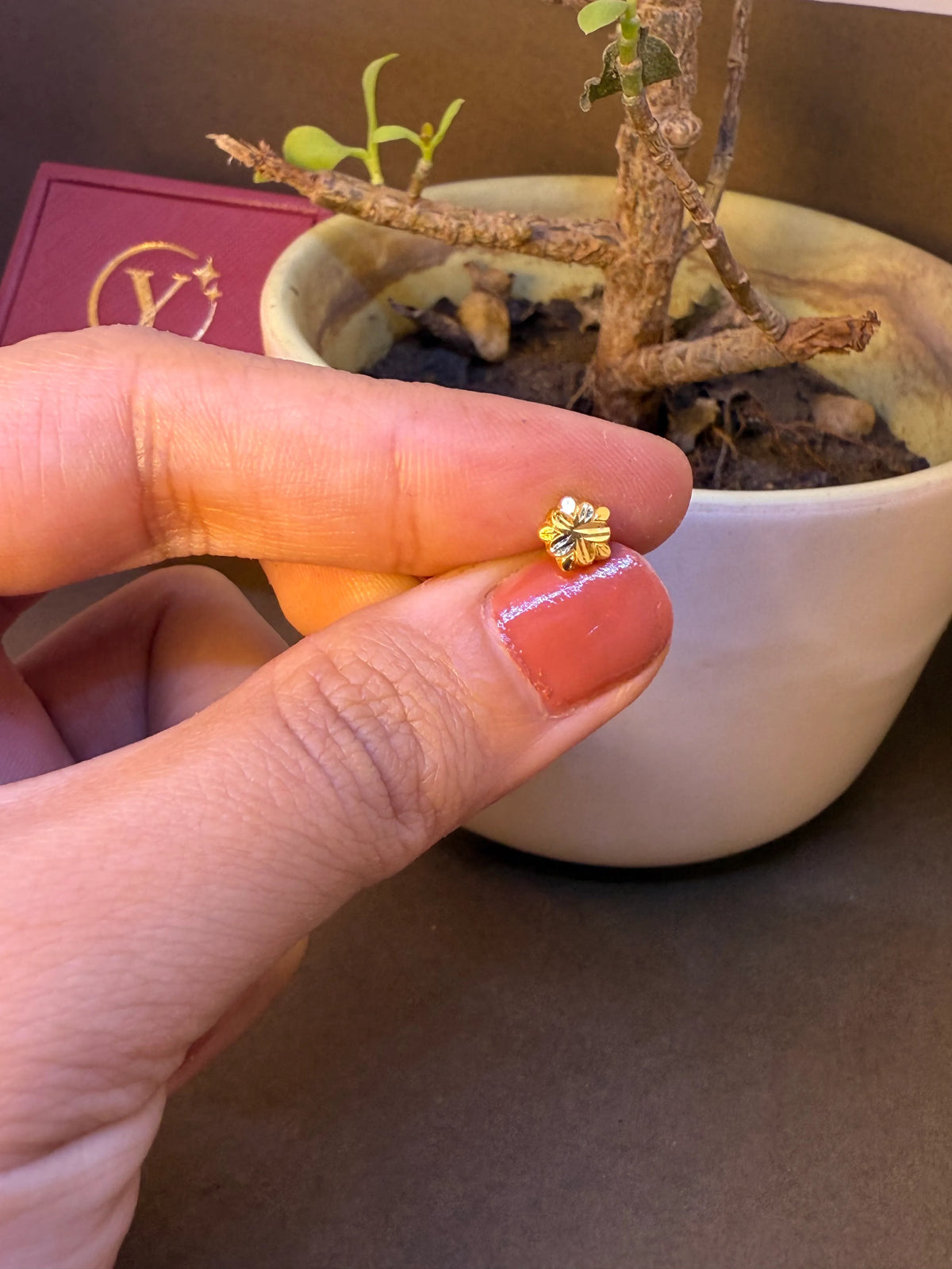 Gold flower-shaped nose pin stud with white stone center held on fingertip