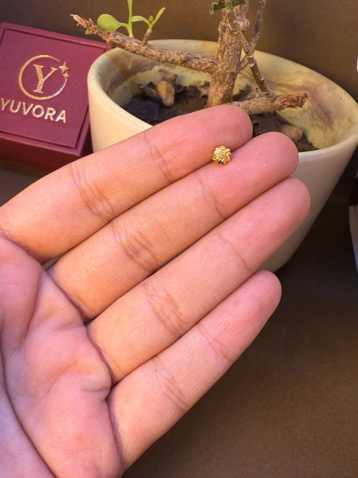 Close-up side view of small gold flower-shaped nose pin stud held between fingers