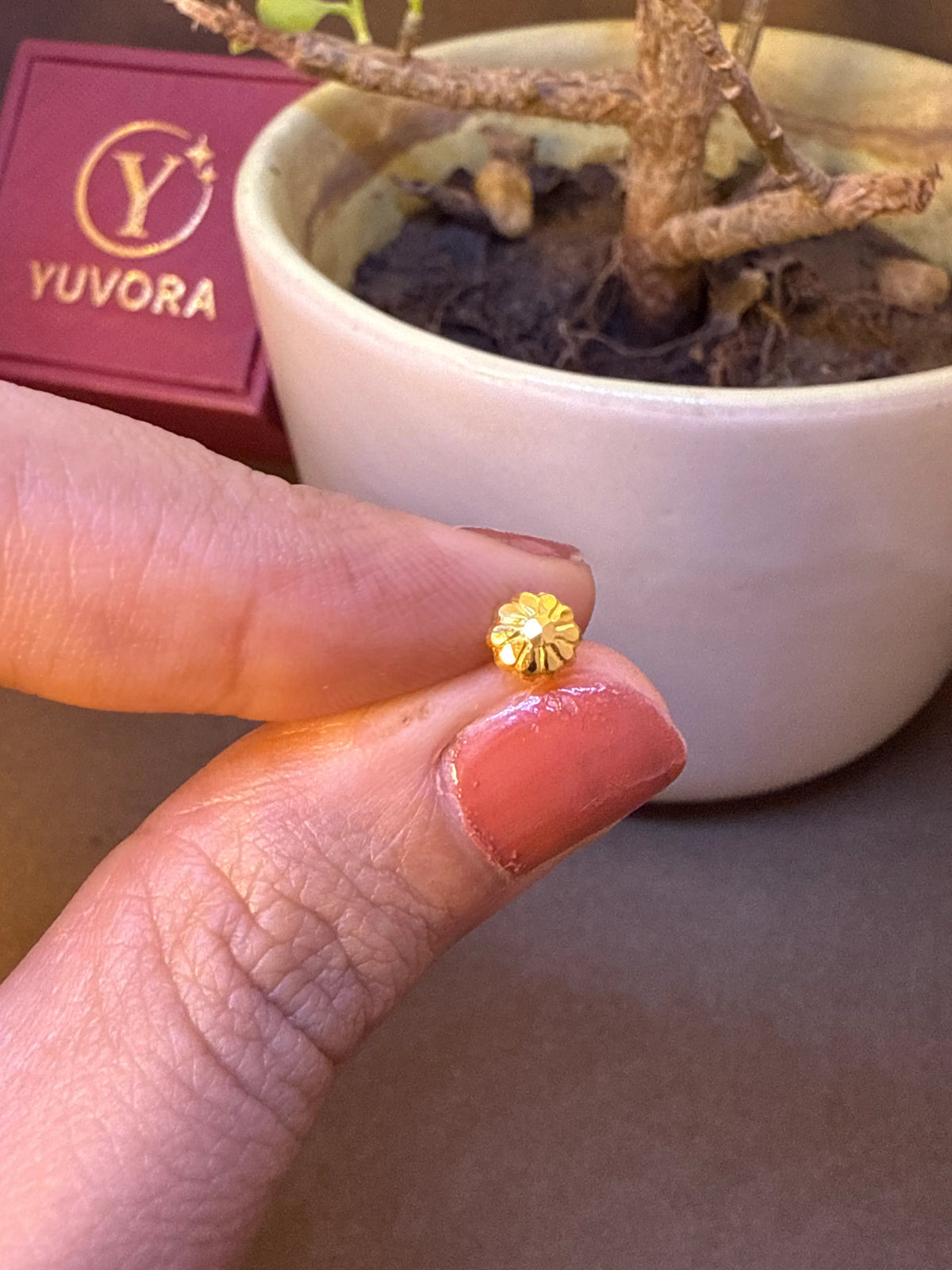 Gold flower-shaped nose pin stud with white stone center held on fingertip