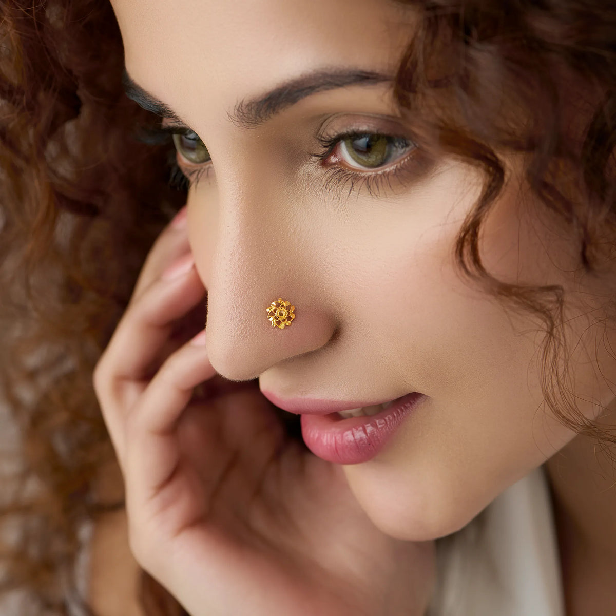 Woman wearing a small gold nose pin shown in a soft side profile with a pleasant smile