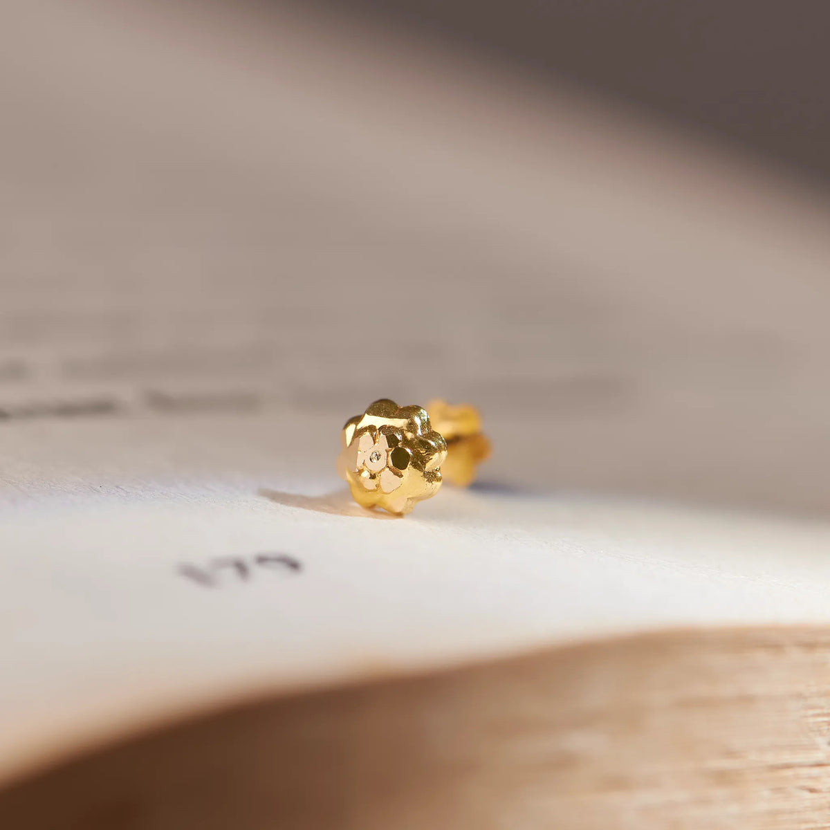 Small textured gold flower-shaped stud earring, close-up