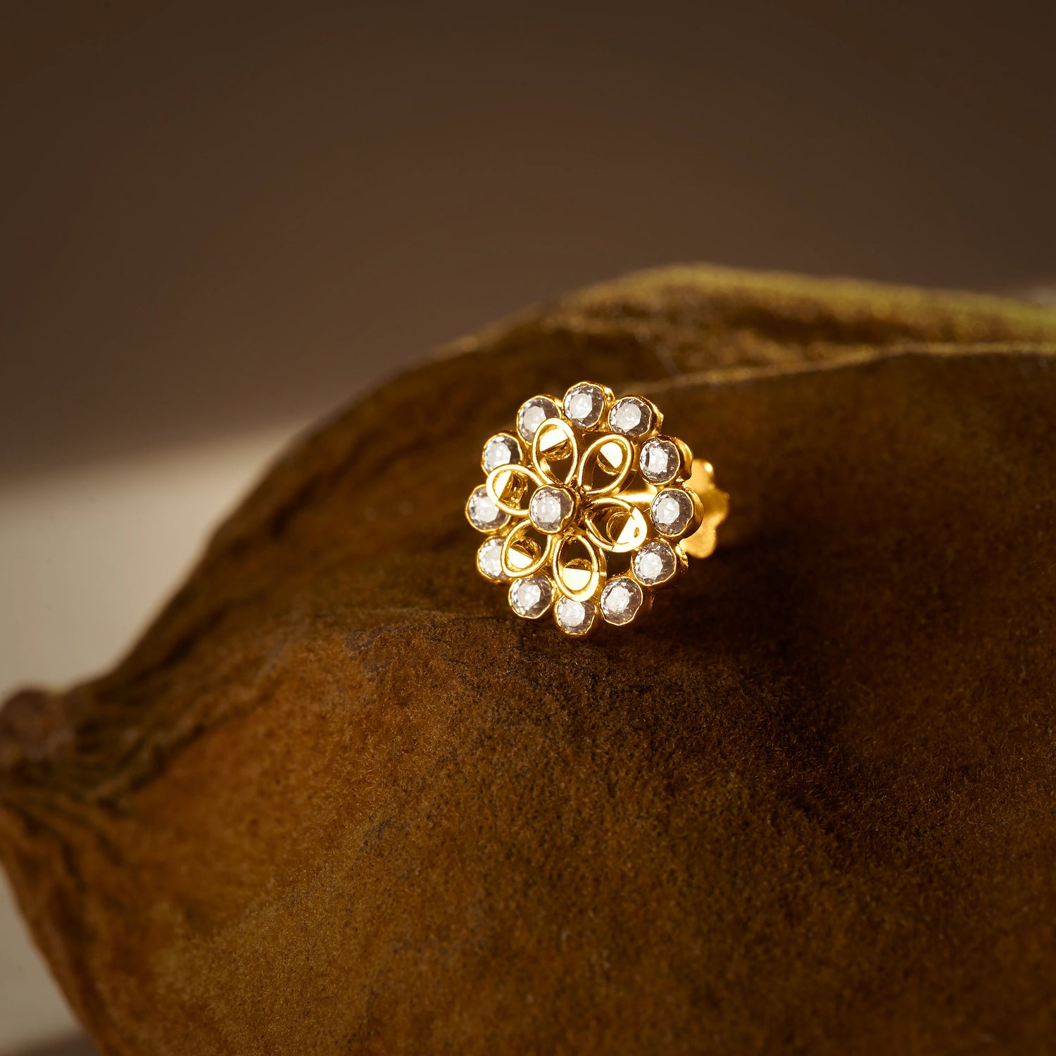 Gold nose pin design with white floral stones on textured surface