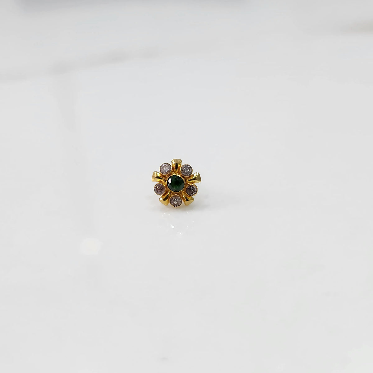 Close-up of flower-shaped gold nose pin with emerald-tone center