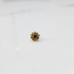 Close-up of flower-shaped gold nose pin with emerald-tone center