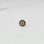 Front view of large gold nose pin with green gemstone petals and purple center stone on white background