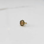 Large gold nose pin with green gemstone petals and purple center stone on white background