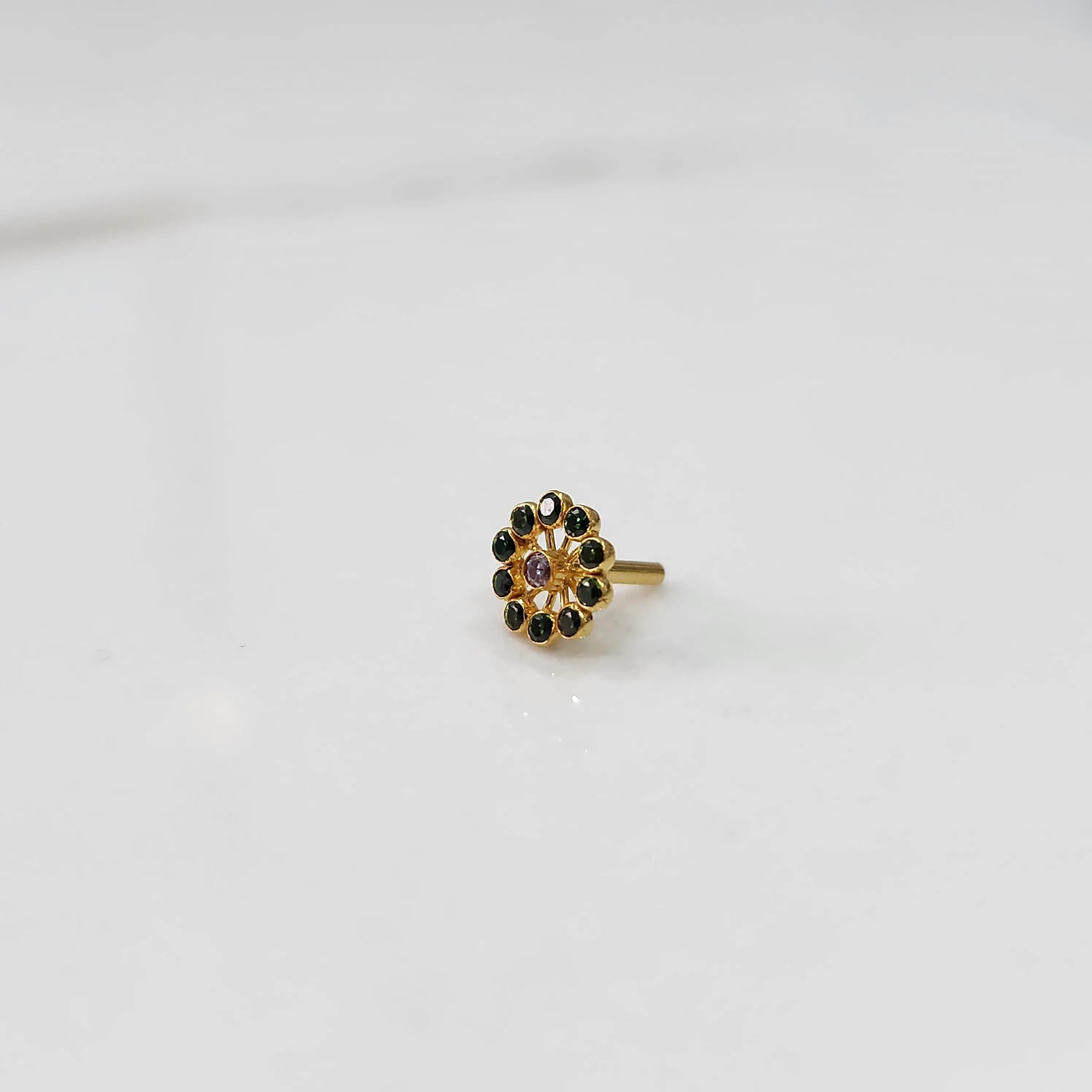 Large gold nose pin with green gemstone petals and purple center stone on white background