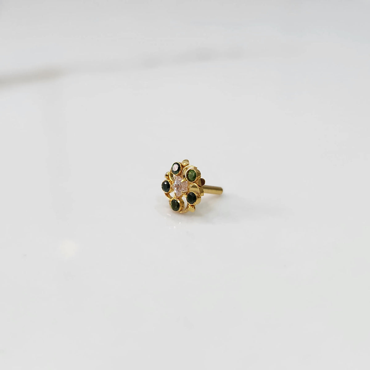 Gold nose pin with green gemstone petals and clear center stone on white background