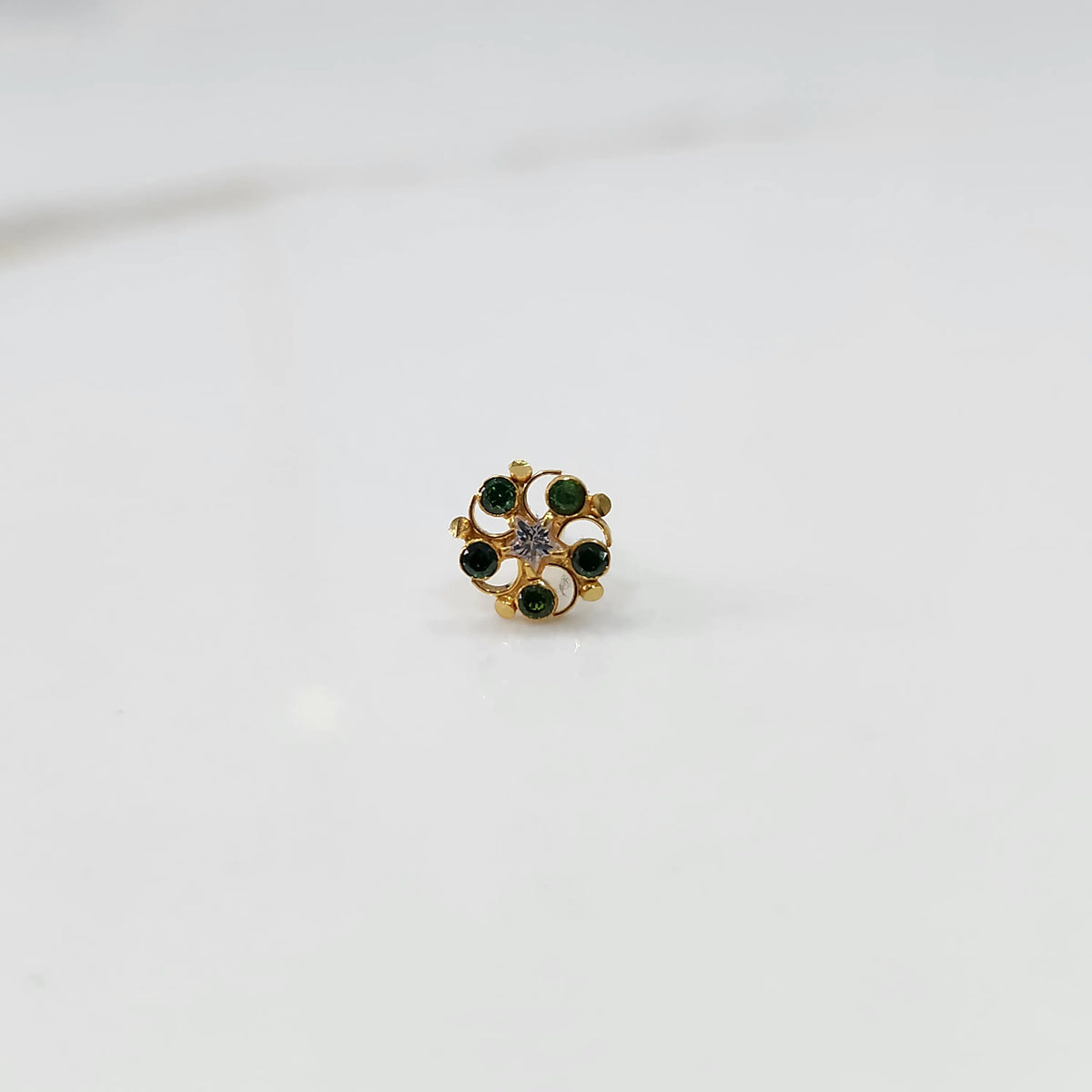 Front view of gold nose pin with green gemstone petals and clear center stone on white background
