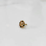 Gold pin nose with compact floral diamond nose pin set with alternating green and purple stones around a white center stone, placed on a white background