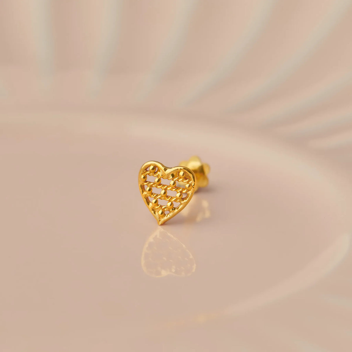 Gold heart-shaped nose stud with textured lattice pattern on beige background