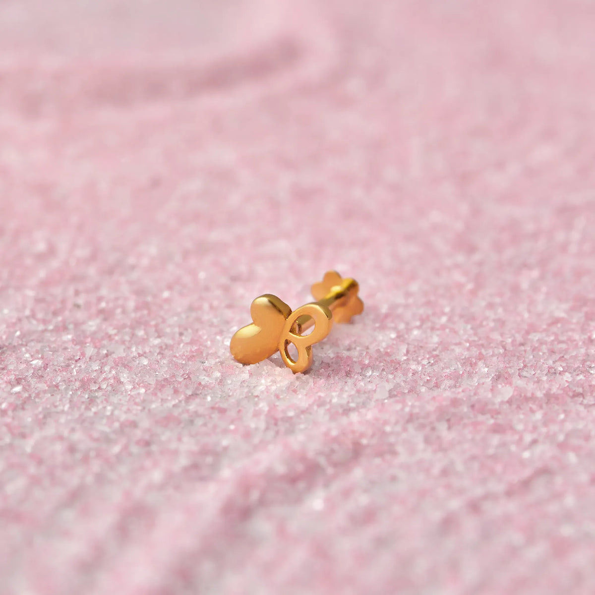 Gold heart-shaped nose stud with looped design on pink glitter background