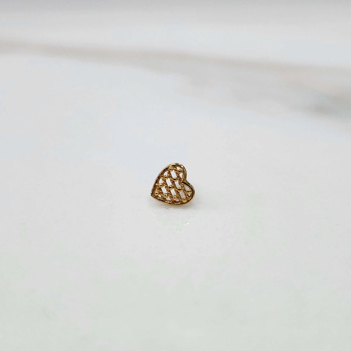 Close up of gold nose stud with woven heart design
