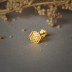 A gold hexagon-shaped stud earring with a jali cutwork pattern, placed on a grey background