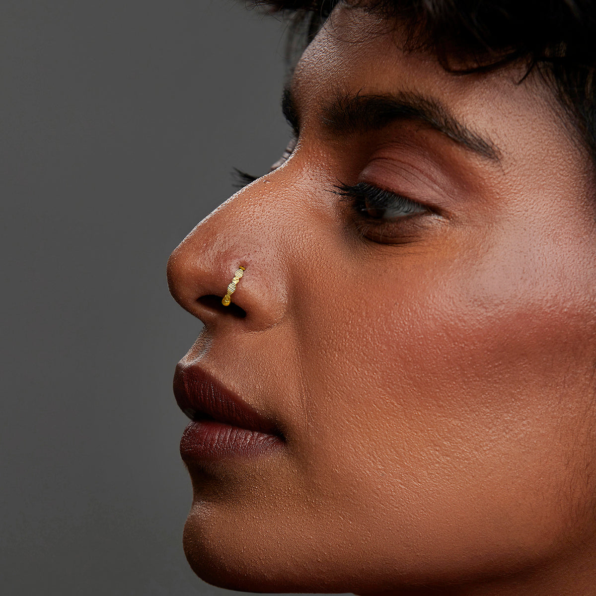 Close-up of a woman wearing a thin gold beaded hoop nose ring