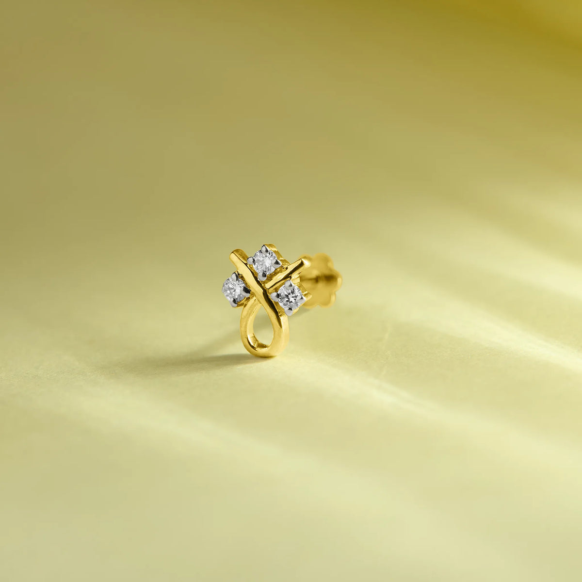 Gold stone nose pin with a floral-inspired design and sparkling white stones placed on a soft light green background.