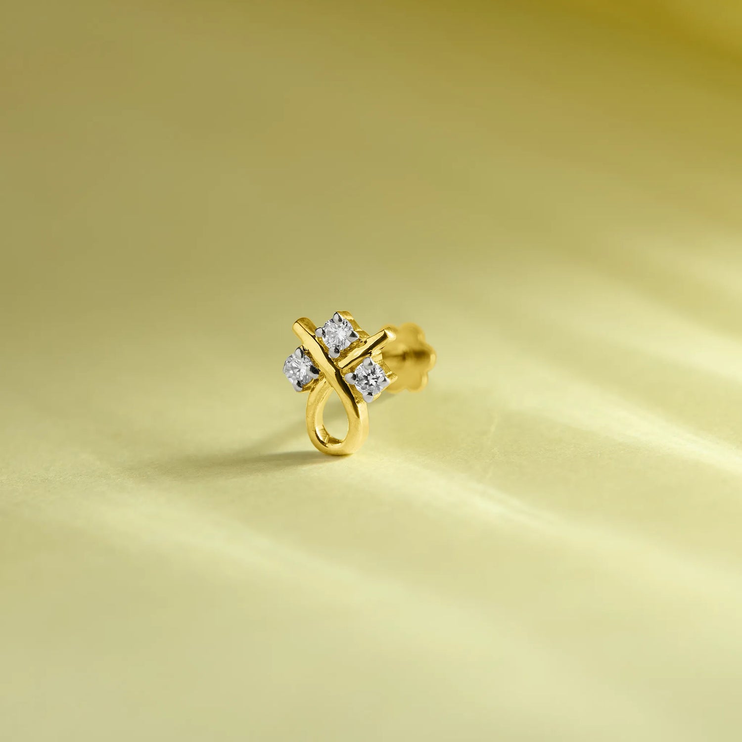 Gold stone nose pin with a floral-inspired design and sparkling white stones placed on a soft light green background.
