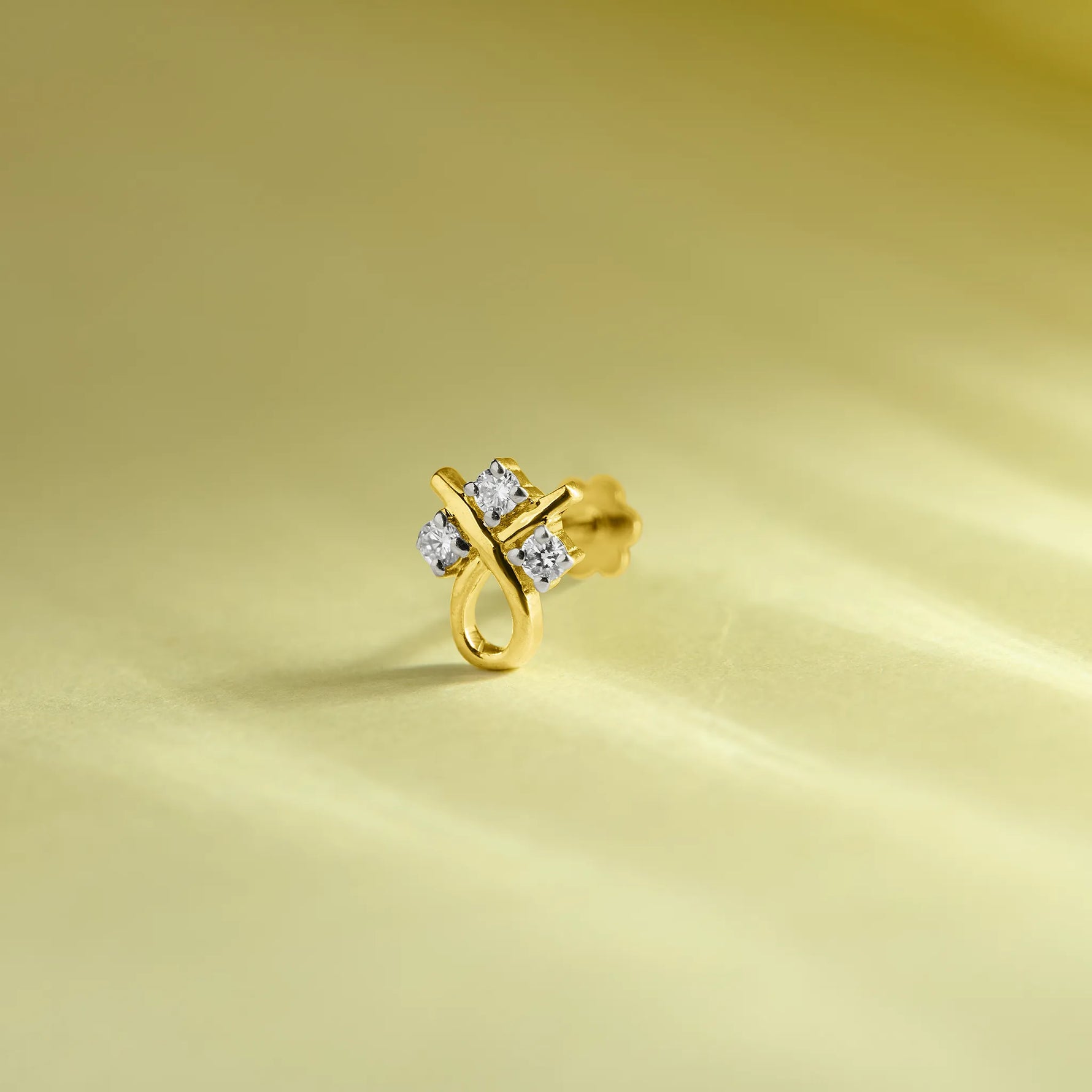 Gold stone nose pin with a floral-inspired design and sparkling white stones placed on a soft light green background.