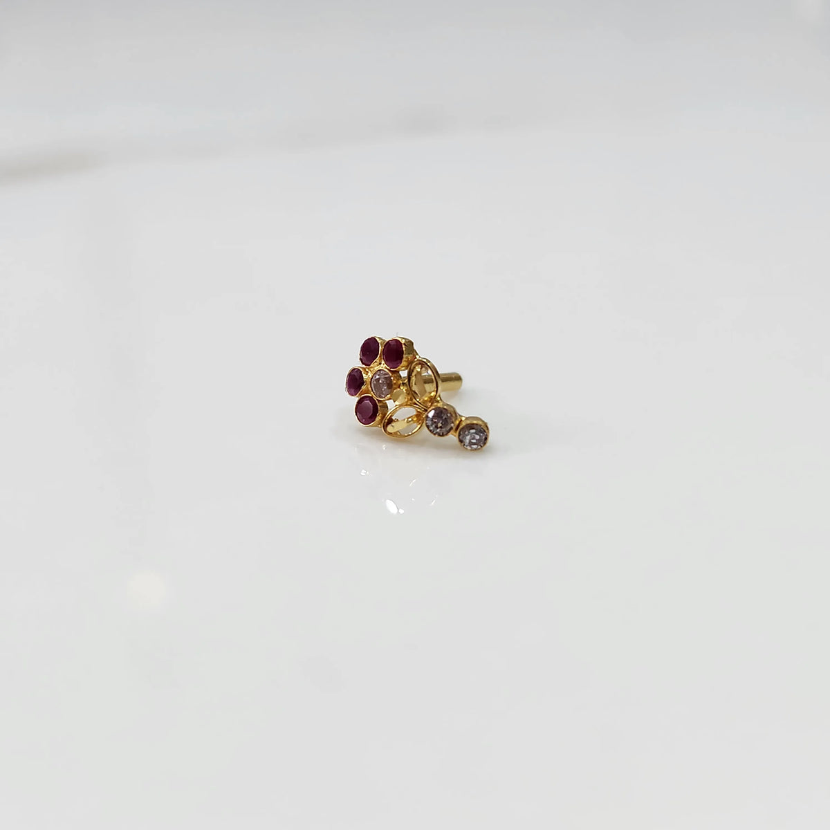 Gold nose pin with magenta gemstone cluster and clear drop-style stone accent on white background