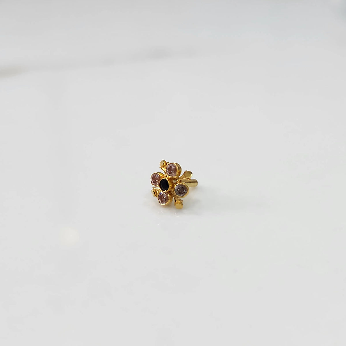 Angled view of gold nose pin with multicolor gemstone flower design on white background