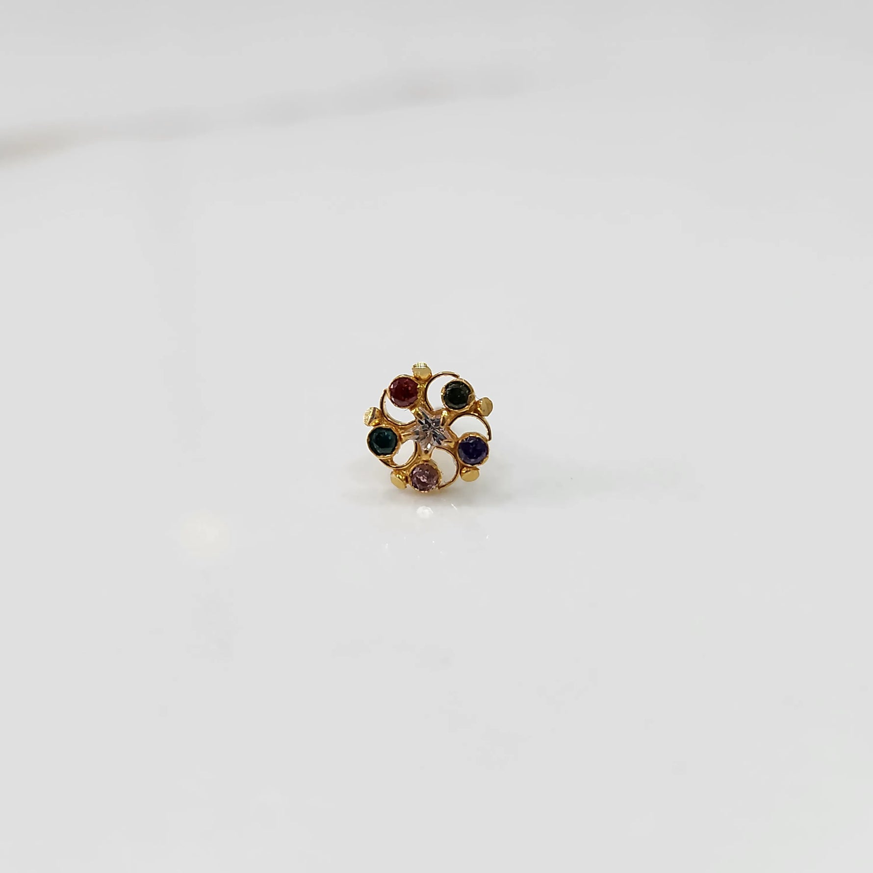 Front view of gold nose pin with multicolor gemstone petals and clear center stone on white background