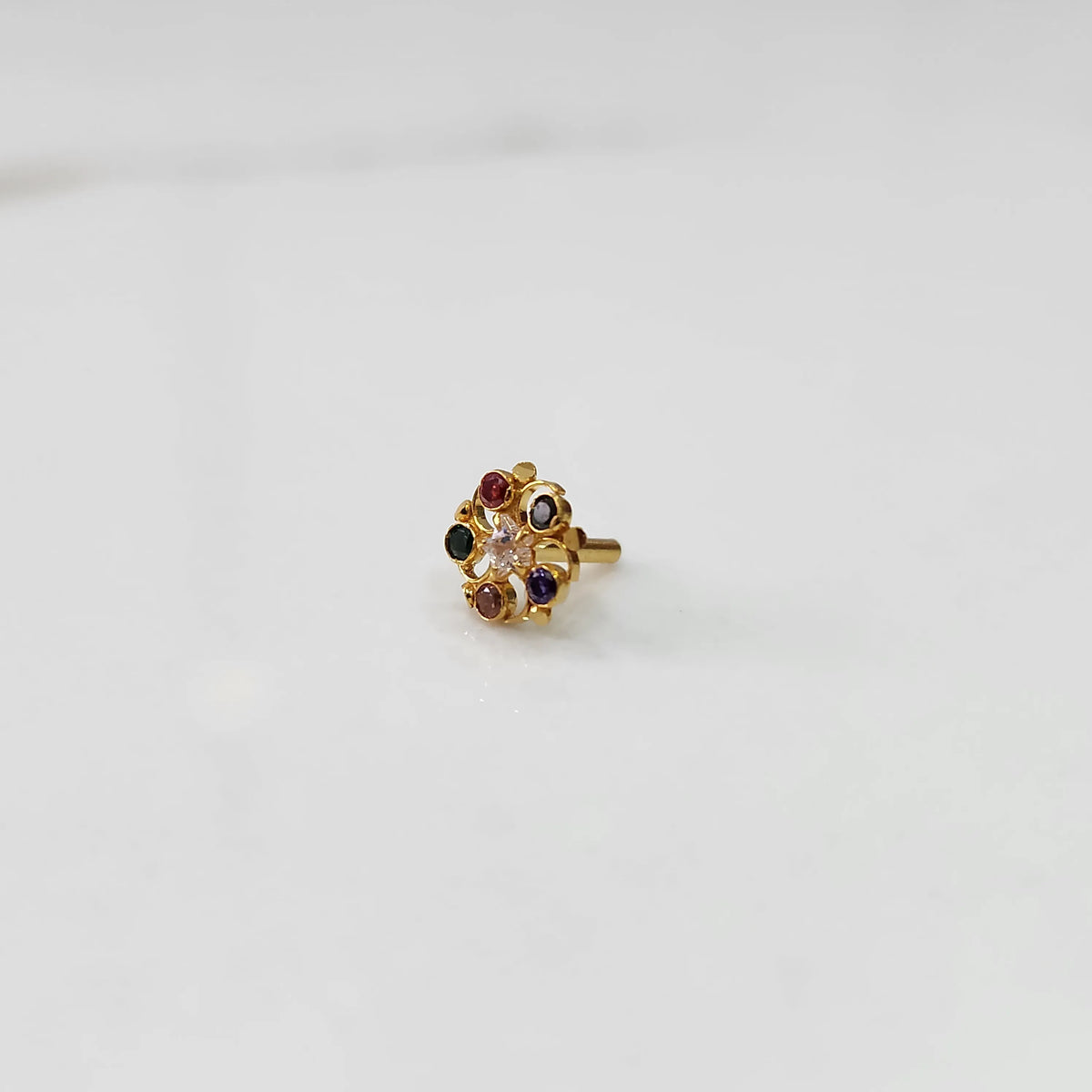 Gold nose pin with multicolor gemstone petals and clear center stone on white background