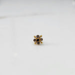 Close-up of gold nose pin with multicolor gemstone flower design on white background