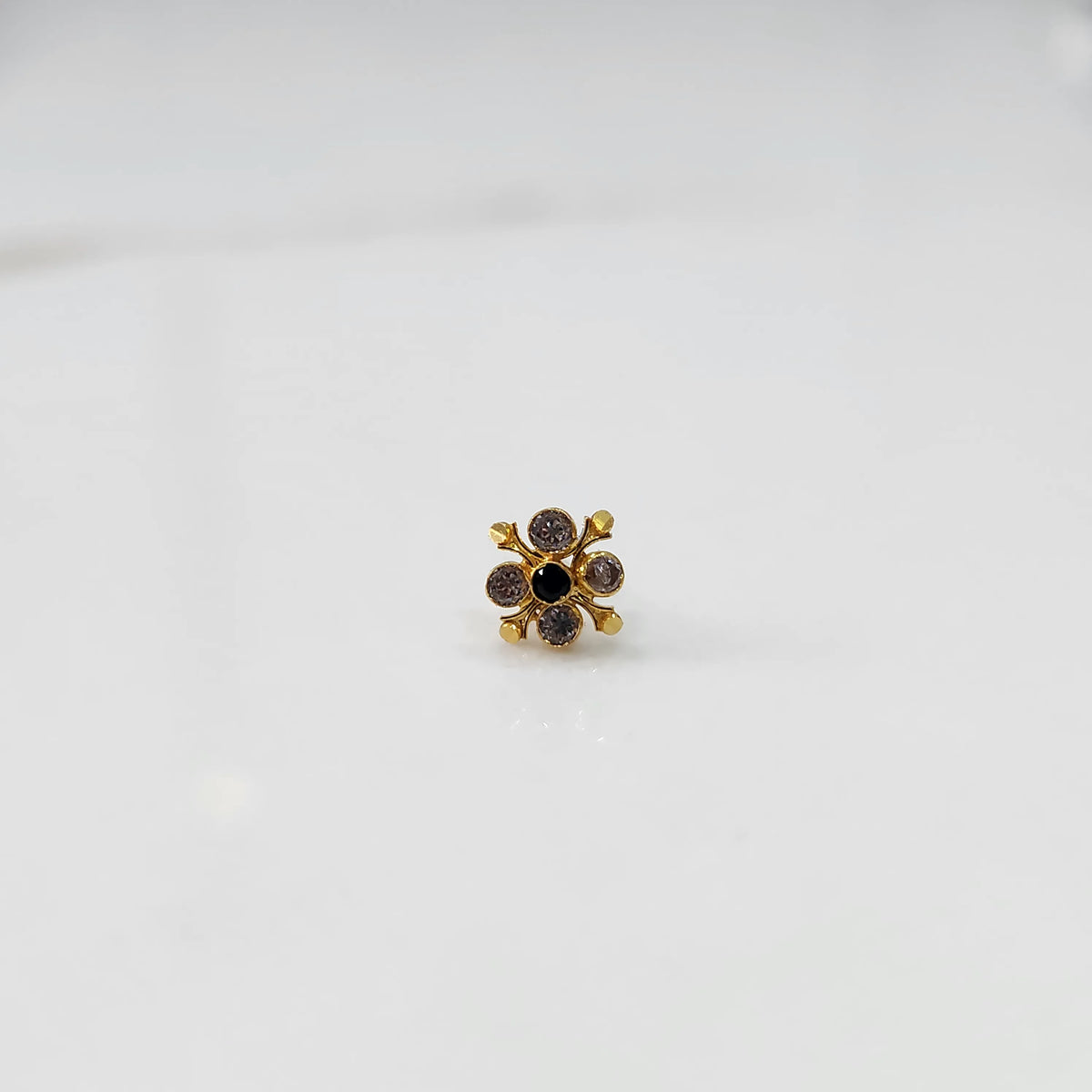 Close-up of gold nose pin with multicolor gemstone flower design on white background
