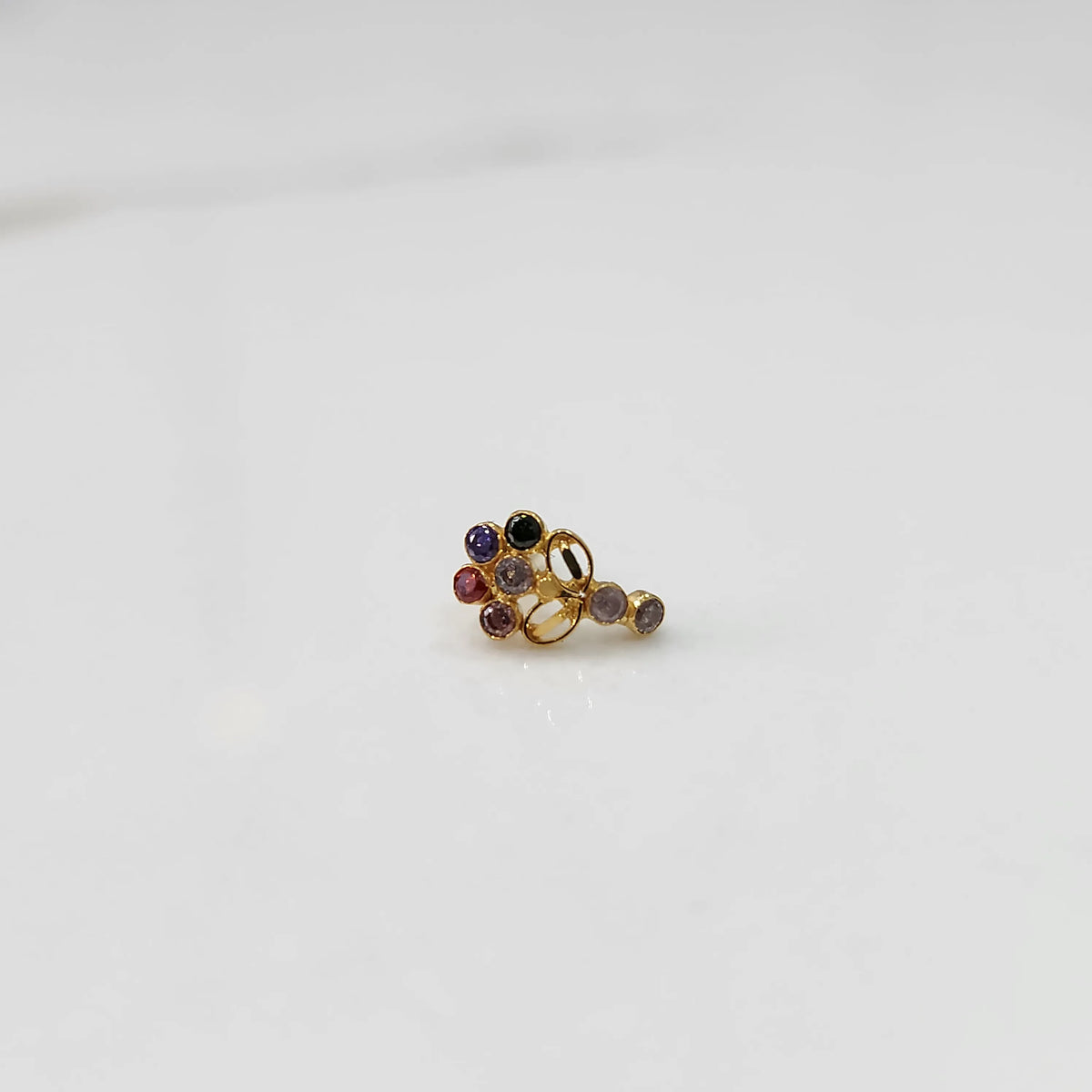Angled view of gold nose pin with multicolor gemstone cluster and drop-style stone accent on white background
