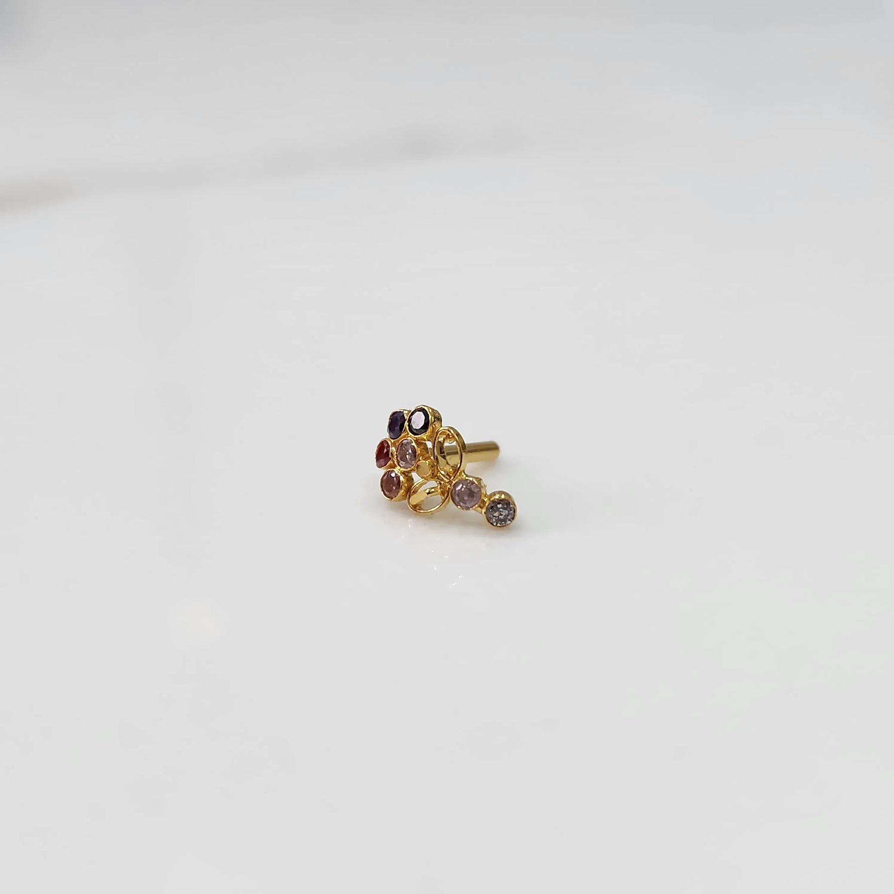 Gold nose pin with multicolor gemstone cluster and drop-style stone accent on white background