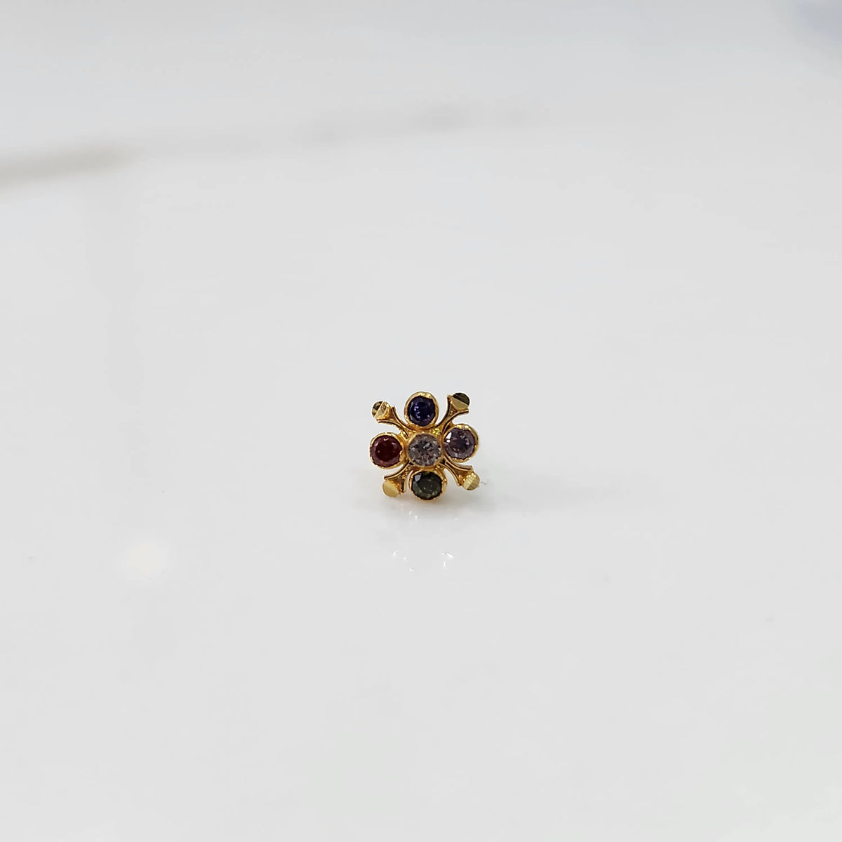 Front view of gold nose pin with multicolor gemstone flower design on white background